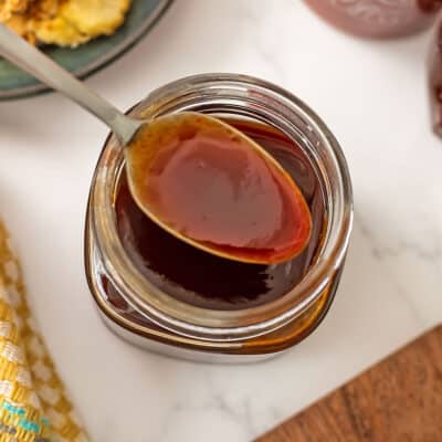 Spoonful of sriracha honey over a glass jar filled with sriracha honey sauce.