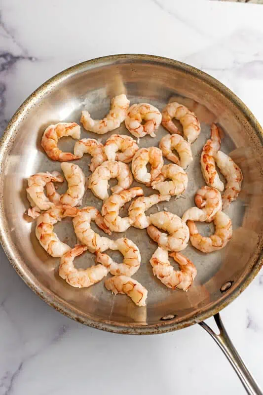 Raw shrimp in a stainless steel skillet.