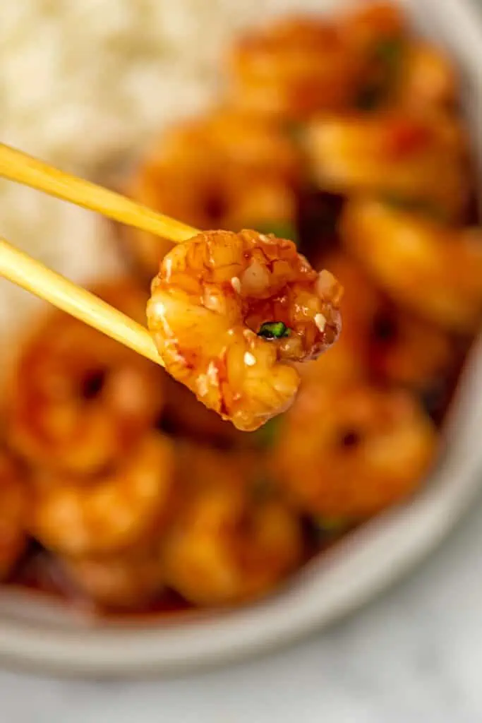 Chopsticks picking up a honey sriracha shrimp over the pan.