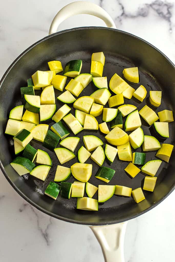 Chopped zucchini and yellow squash in cast iron skillet.