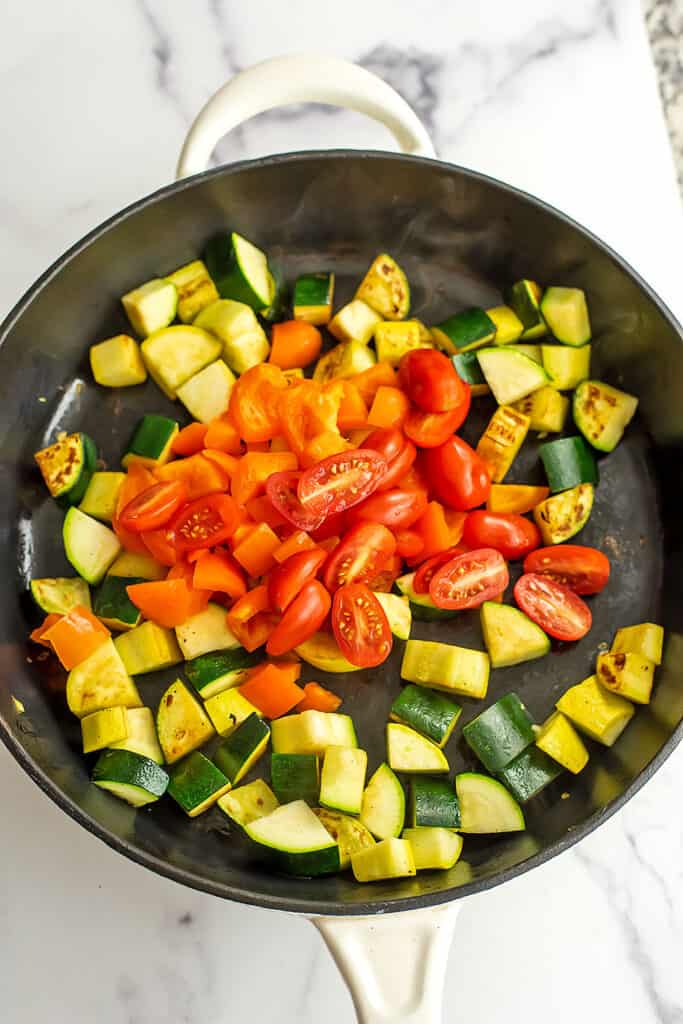 Bell pepper and tomatoes in skillet with cooked squash.
