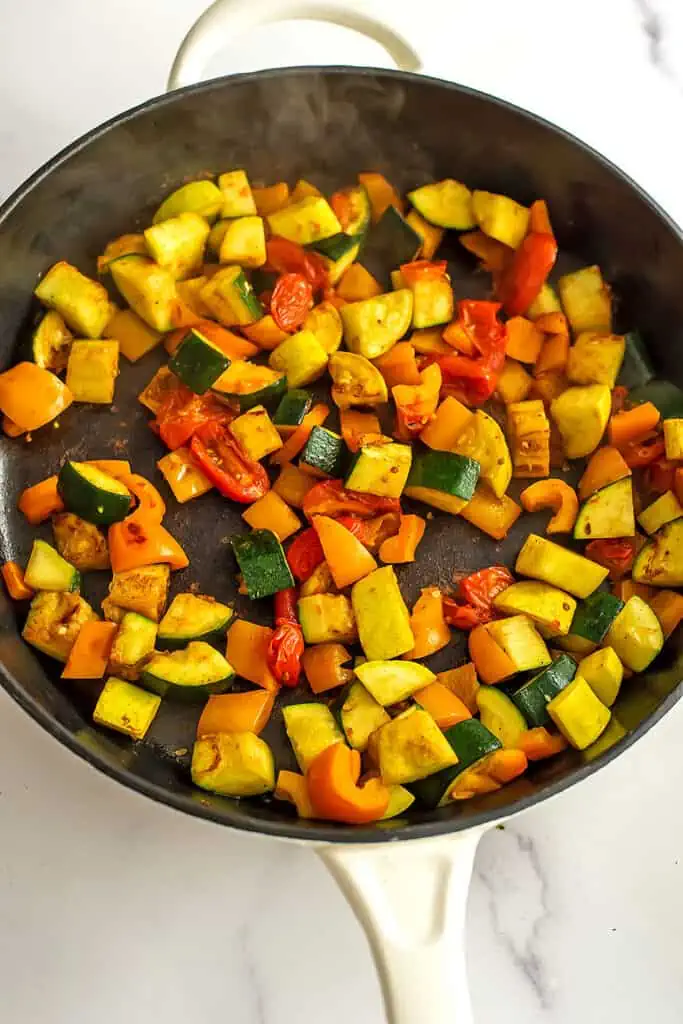 Cooked zucchini, squash, bell peppers and tomato in a large skillet.