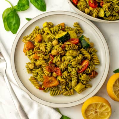 White plate full of pesto vegetable pasta, fork on the side.
