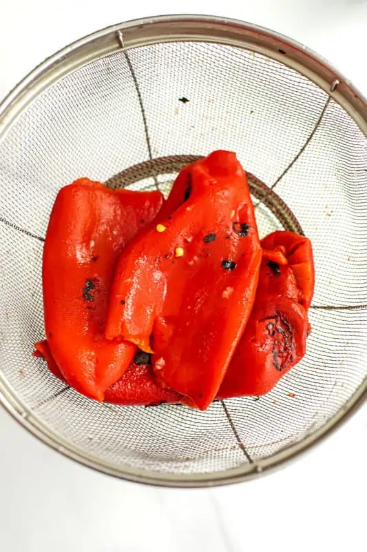 Roasted red peppers in a mesh strainer.