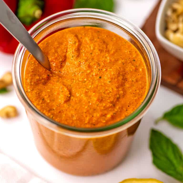 Roasted red pepper pesto in a jar with a spoon in the jar.