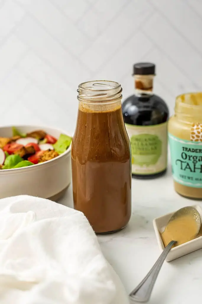 Tahini balsamic dressing in a glass bottle with balsamic vinegar in background.