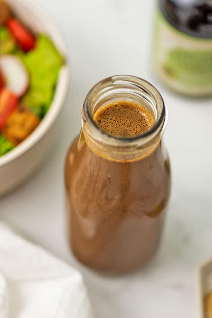 Balsamic tahini dressing in a bottle with salad in the background.