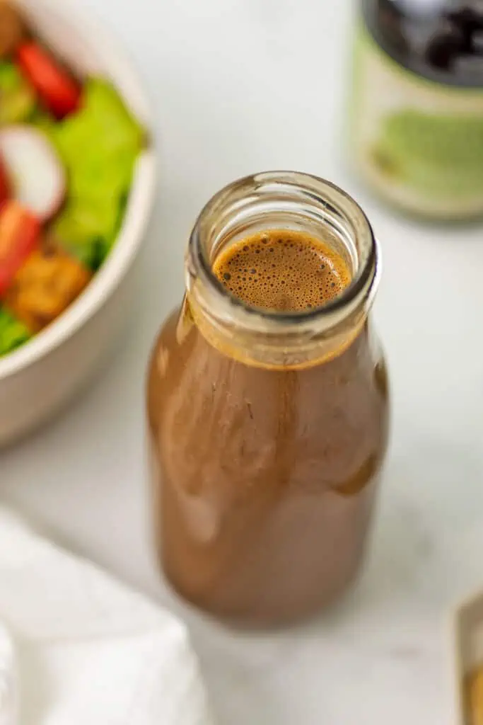 Balsamic tahini dressing in a bottle with salad in the background.
