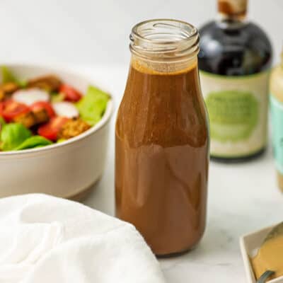 Glass bottle filled with balsamic tahini dressing with white napkin.