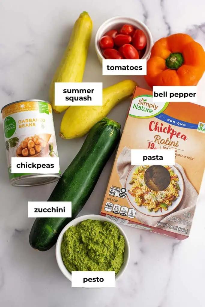 Ingredients to make vegetable pesto pasta on a marble countertop.