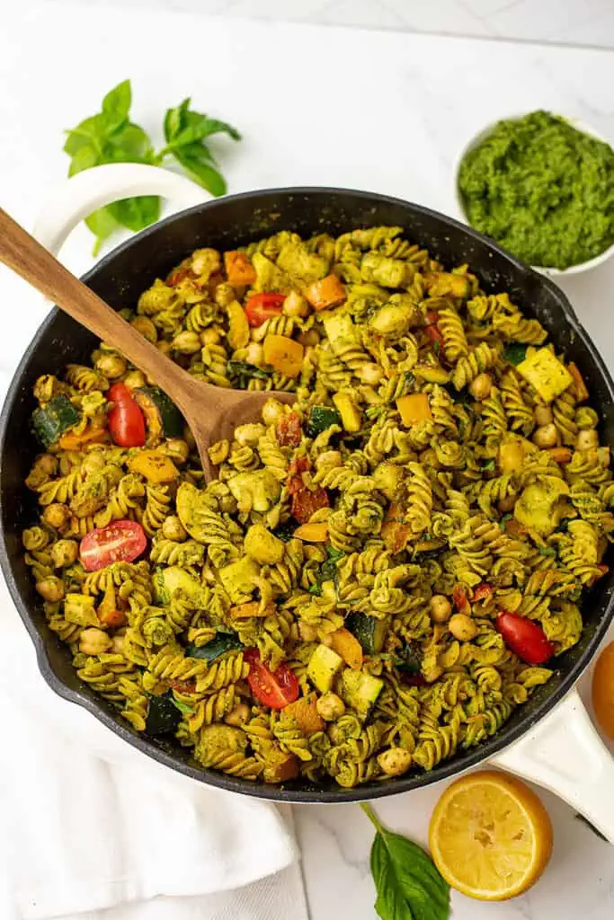 Skillet of veggie pesto pasta with a wooden spoon resting in the skillet. 