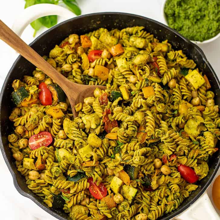 Skillet of veggie pesto pasta with a wooden spoon resting in the skillet.
