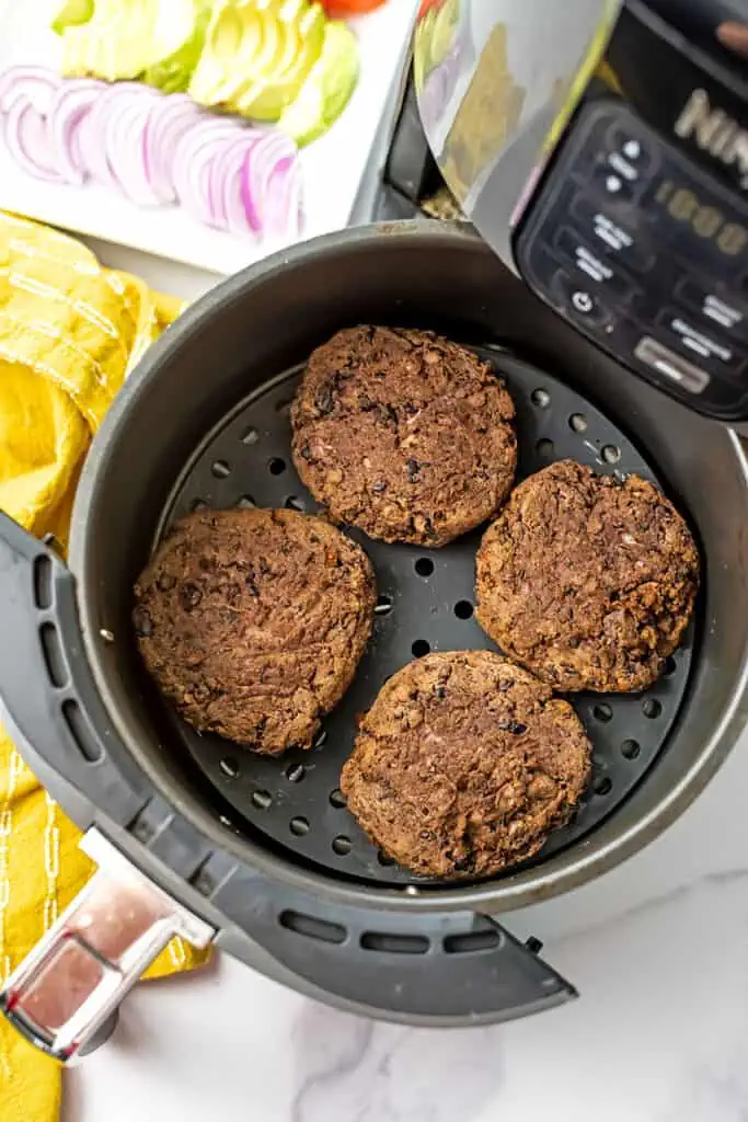 Black bean burgers in air fryer basket with yellow napkin on the side.