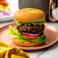 Black bean burger on a bun and toppings on a pink plate.