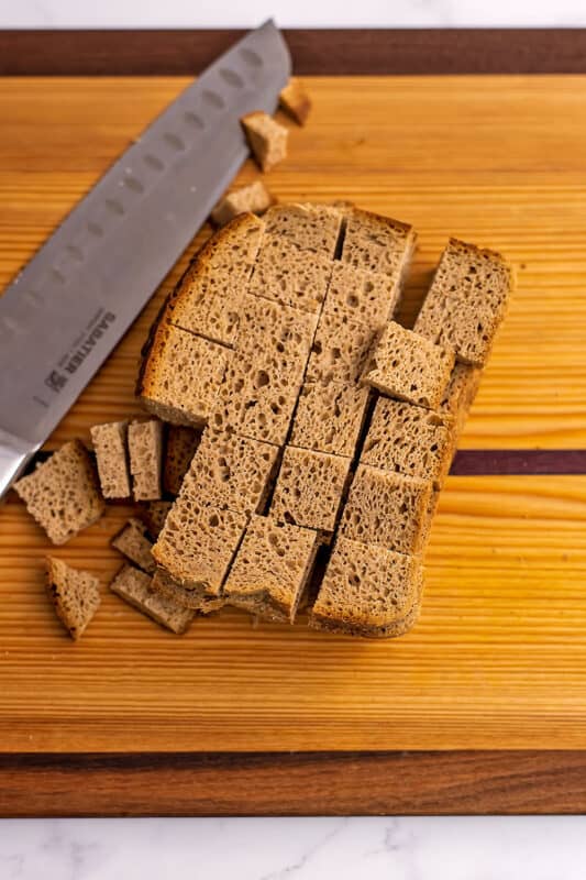 Gluten free bread cut into cubes on a wood cutting board.