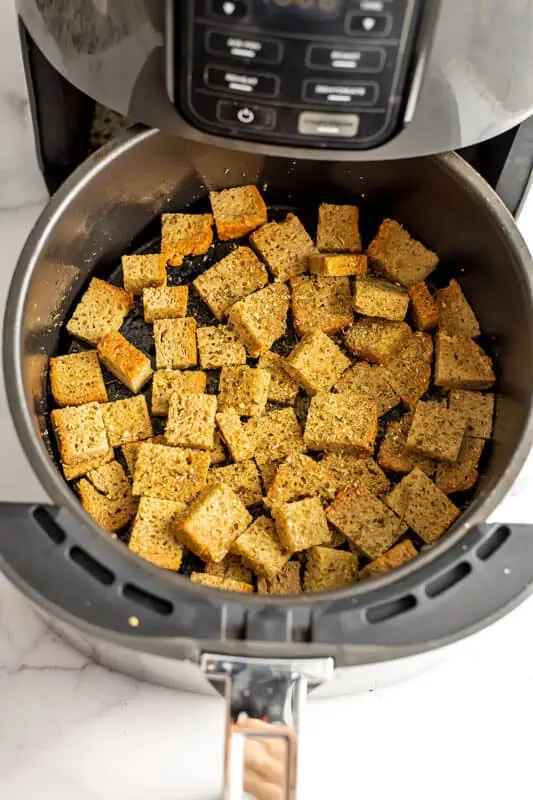 Bread cubes with spices in air fryer basket before cooking.