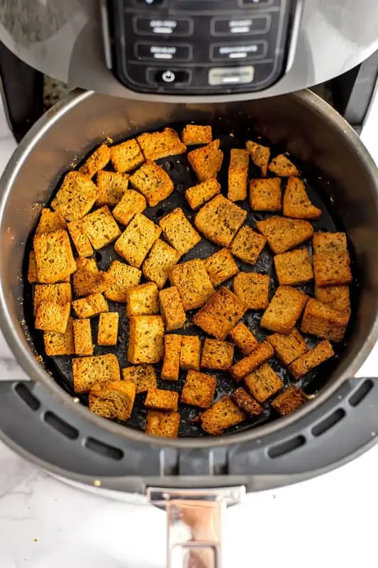 Crispy gluten free croutons in air fryer basket after cooking.
