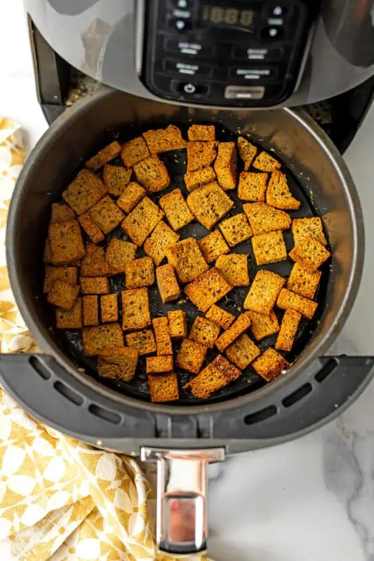 Air fryer basket filled with gluten free croutons with yellow napkin on side.