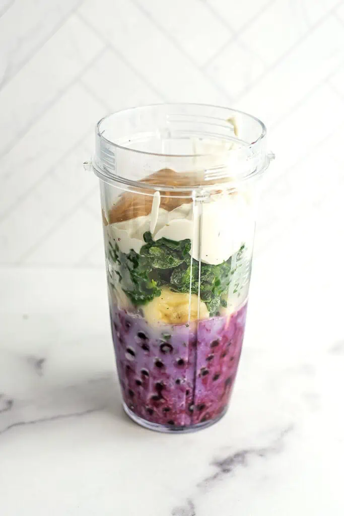 Blueberry banana spinach smoothie ingredients in a blender cup before blending.