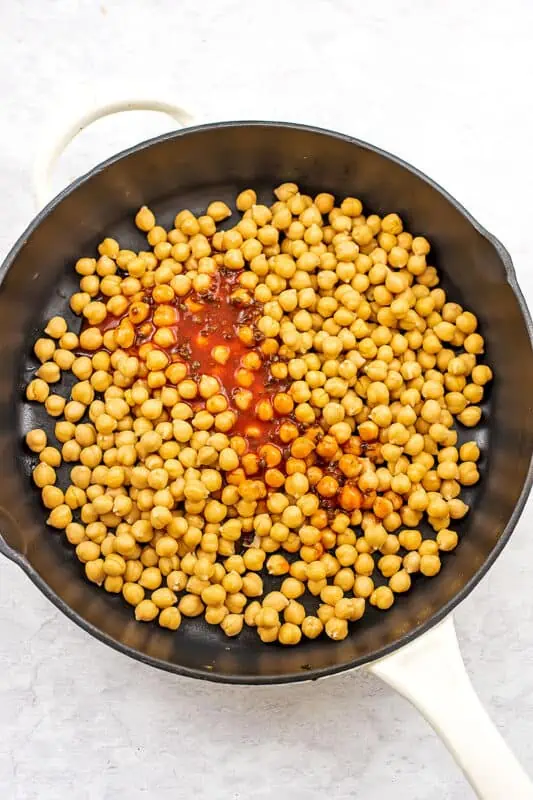 Buffalo sauce poured over chickpeas in a skillet.