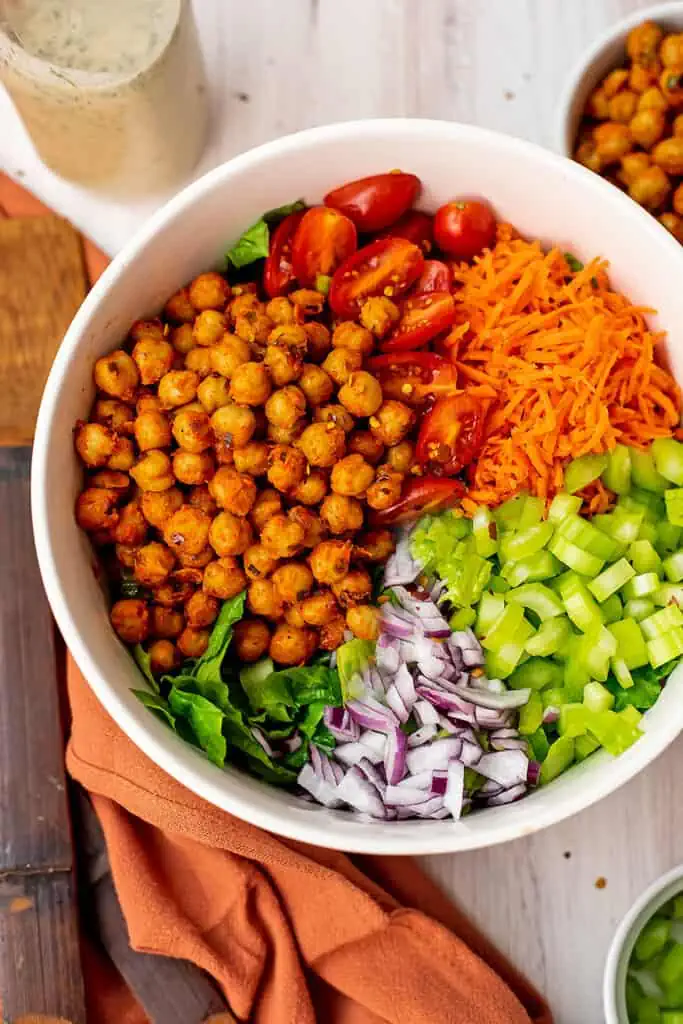 Ingredients to make buffalo chickpea salad in a large white bowl.
