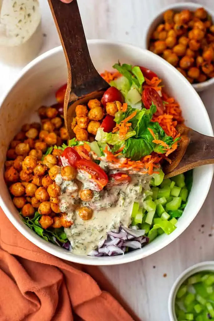 Two spoons stirring up buffalo chickpea salad with tahini ranch dressing.