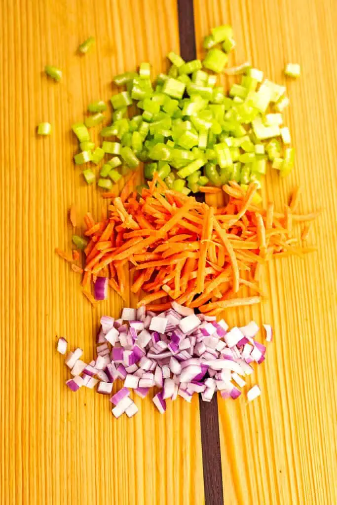 Chopped red onion, celery and carrots on a wooden cutting board.