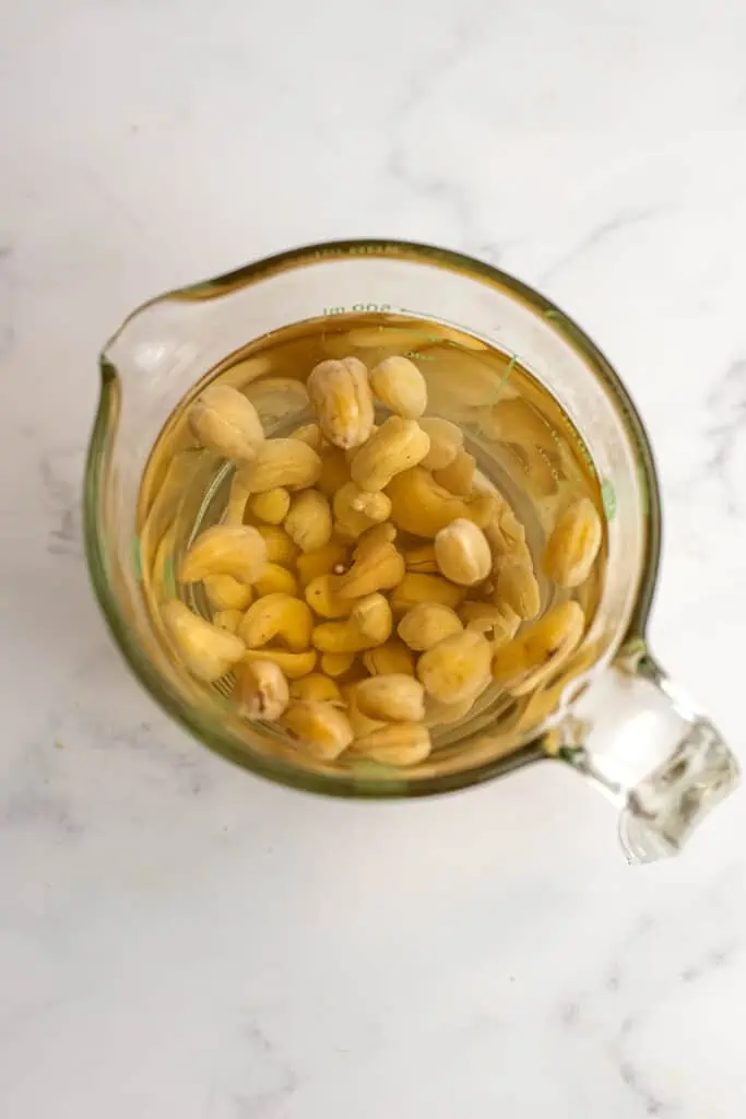 Cashews soaking in hot water in a glass measuring cup.