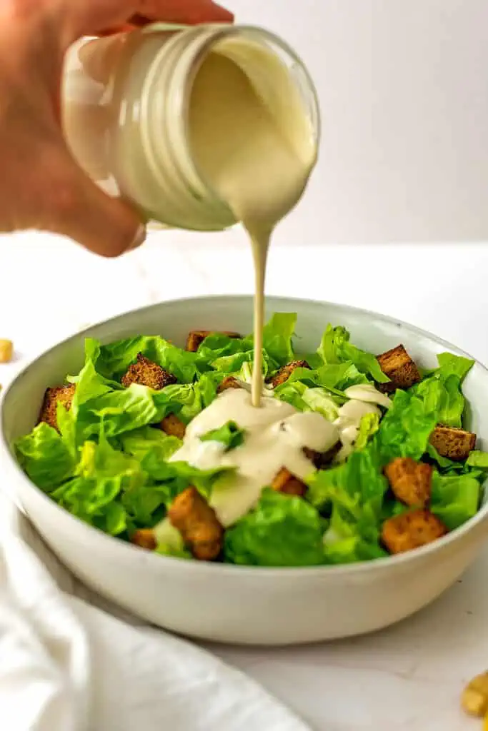 Caesar cashew dressing being poured over salad greens.