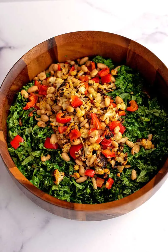 Roasted cauliflower, white beans and red pepper on top of bowl of kale.