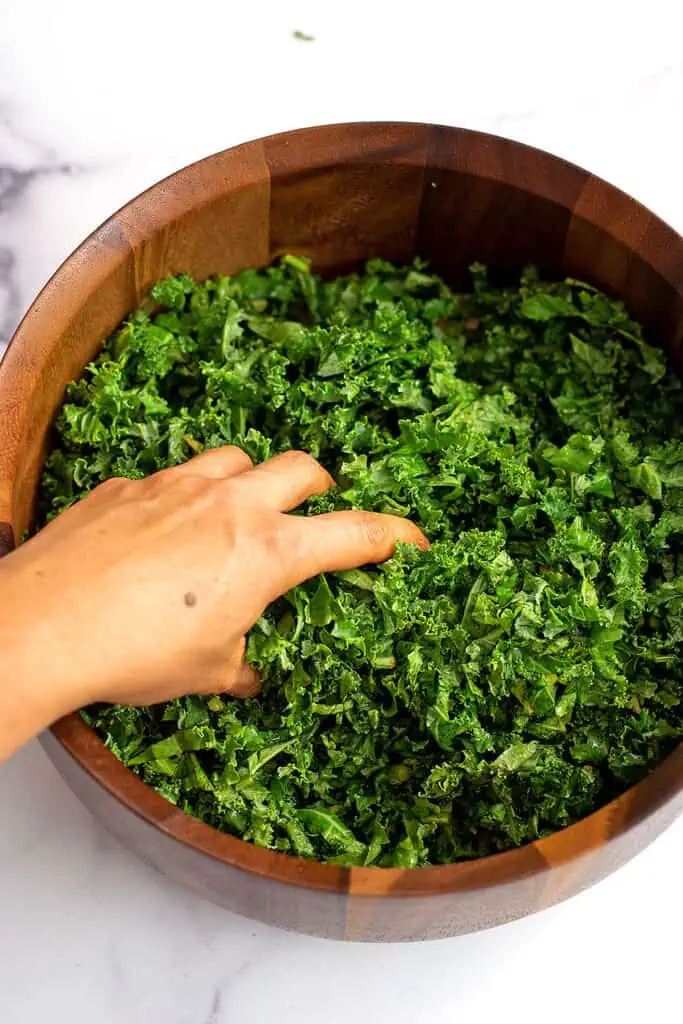 Hand massage balsamic vinegar into kale in wood bowl.