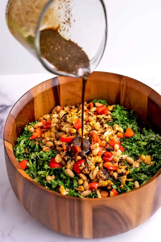 Balsamic dressing being poured over bowl of kale salad.