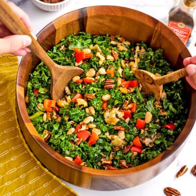 Salad tongs tossing the kale cauliflower salad in wood bowl.
