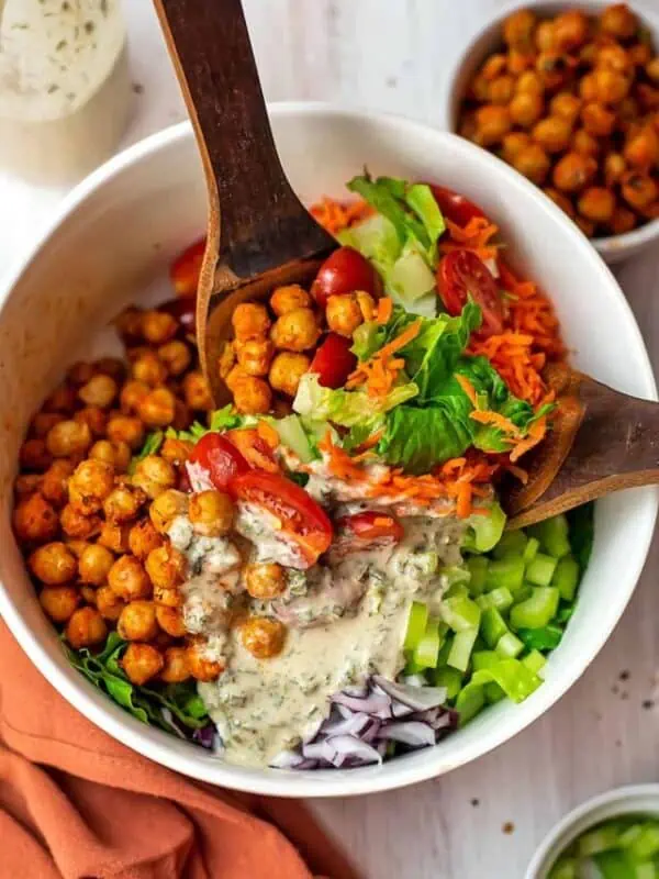 Two spoons stirring up buffalo chickpea salad with tahini ranch dressing.