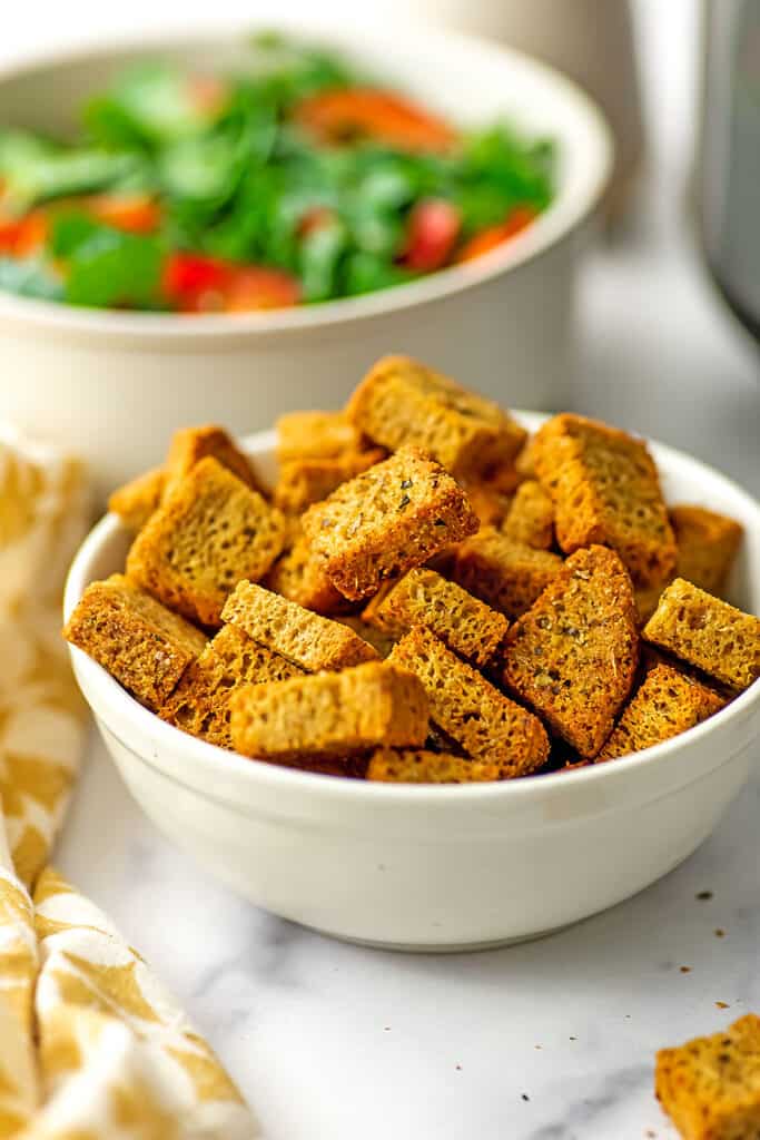 Gluten free croutons in a white bowl with salad in background.