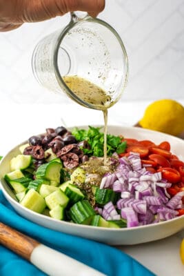 Mediterranean cucumber tomato salad with lemon vinaigrette being poured on top.