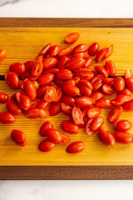 Cherry tomatoes cut in half on a cutting board for Mediterranean tomato cucumber salad.