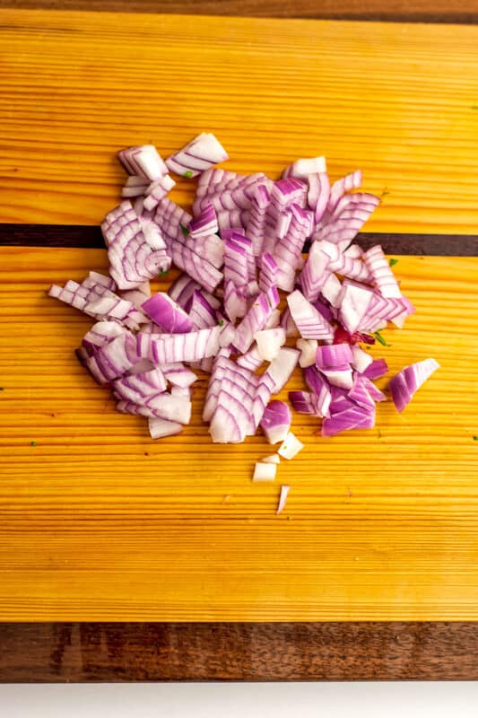 Finely chopped red onion on wood cutting board.