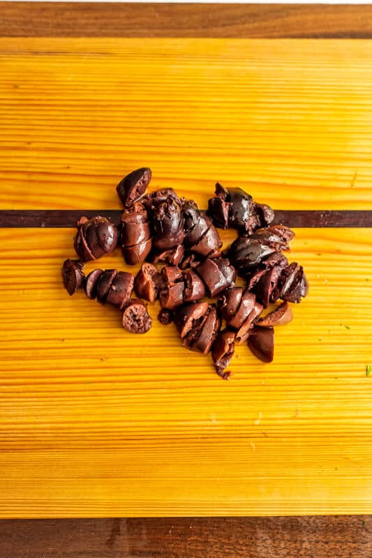 Finely chopped kalamata olives on wood cutting board.
