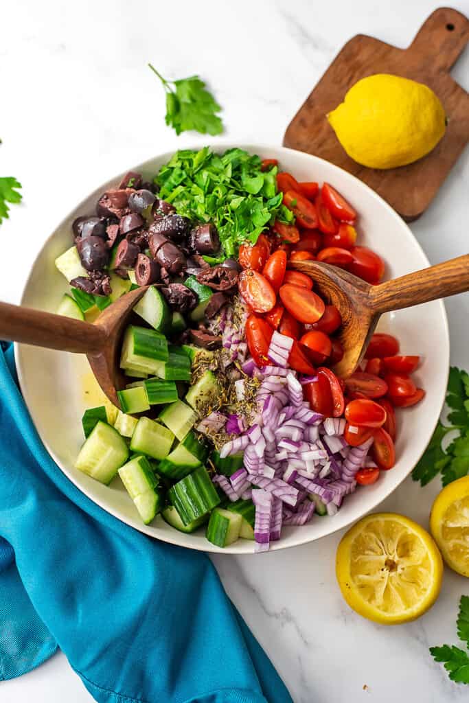 Mediterranean tomato cucumber salad being served with wooden salad servers.
