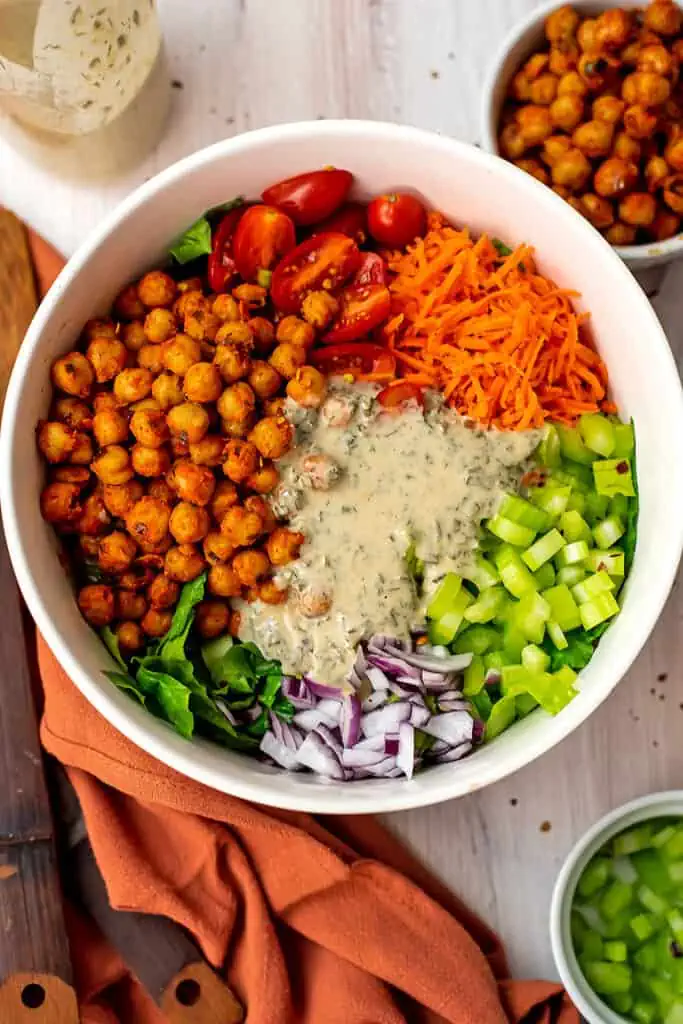 Tahini ranch dressing poured over buffalo chickpea salad ingredients.