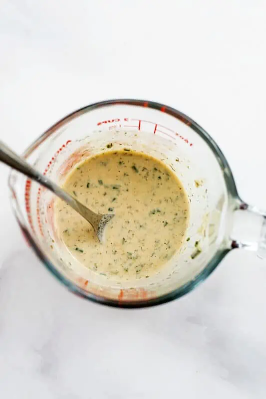 Tahini ranch dressing a glass measuring cup after stirring.
