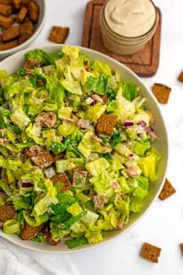 Large white bowl filled with caesar tuna salad with croutons on side.