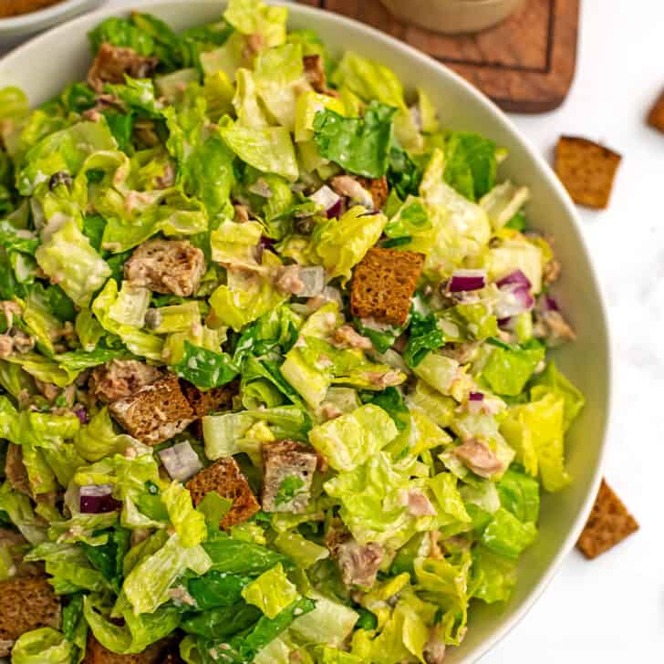 Large white bowl filled with caesar tuna salad with croutons on side.