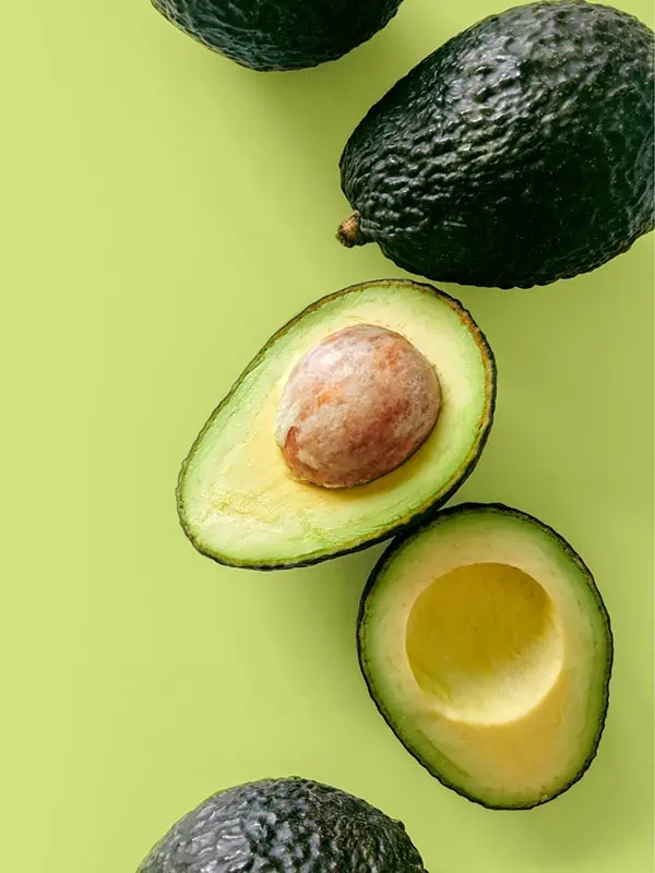 An avocado cut in half on a green surface.