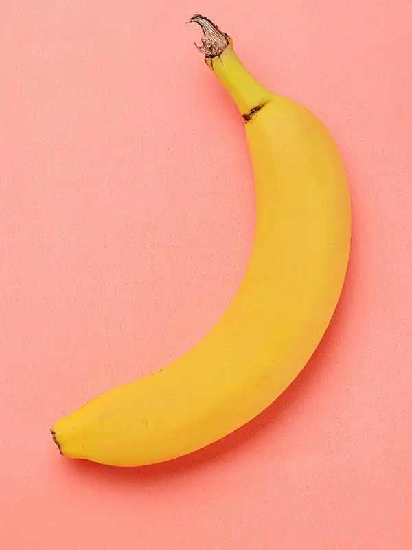 A ripe yellow banana sitting on a pink surface.