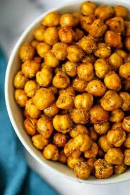 Air fryer roasted chickpeas in a large white bowl next to a teal napkin.