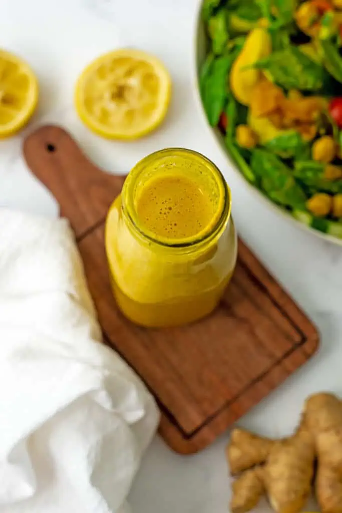 Turmeric salad dressing in a bottle with garlic and lemons around it.