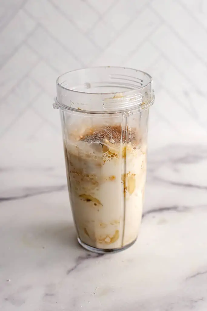 Banana cinnamon smoothie ingredients in a large blender cup before all ingredients have been blended.