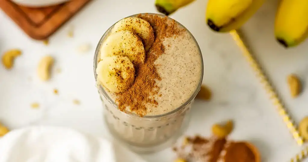 Cinnamon smoothie in a tall glass with cinnamon and bananas added to the top.